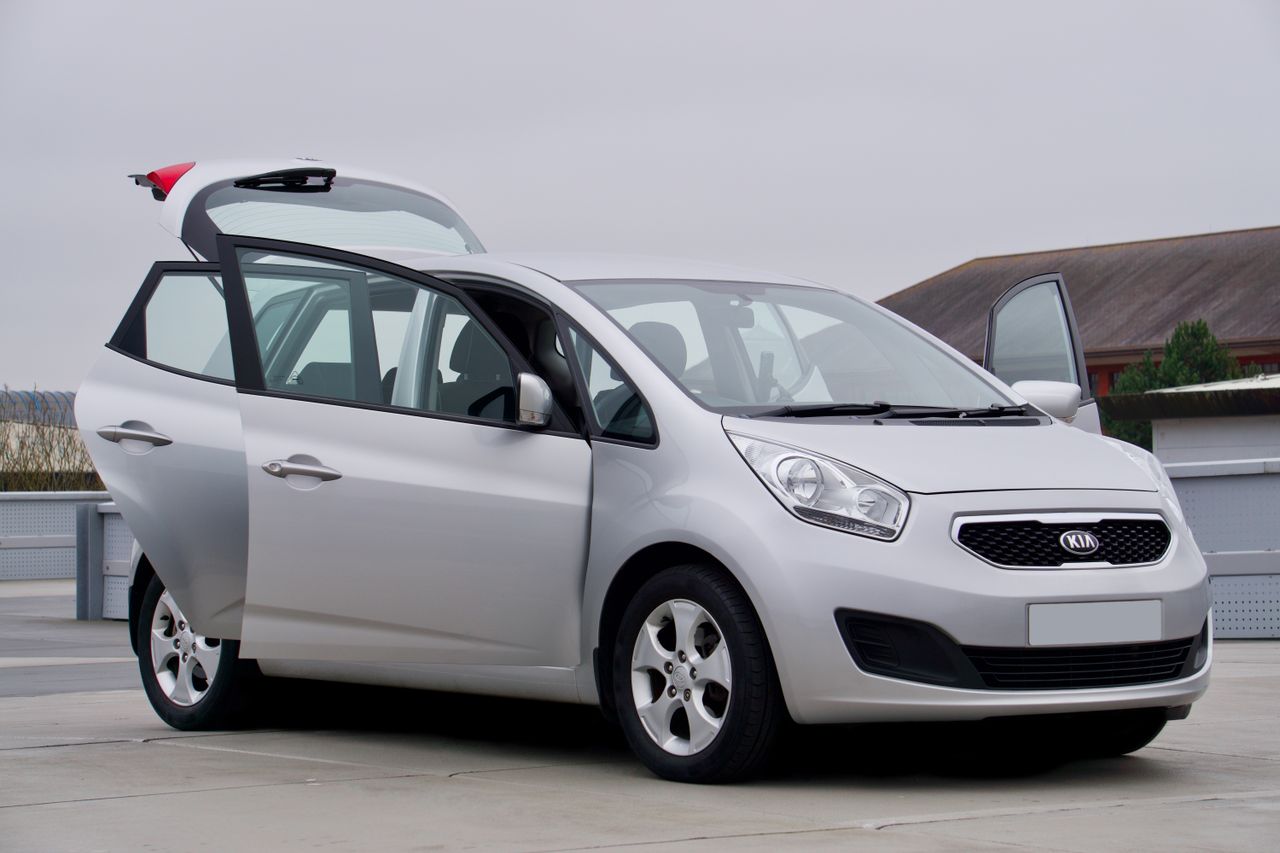 Silver Kia car with open doors parked on pavement, showcasing vehicle design.